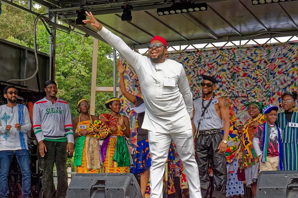 Man in white outfit performing energetically on stage at an African cultural festival.
