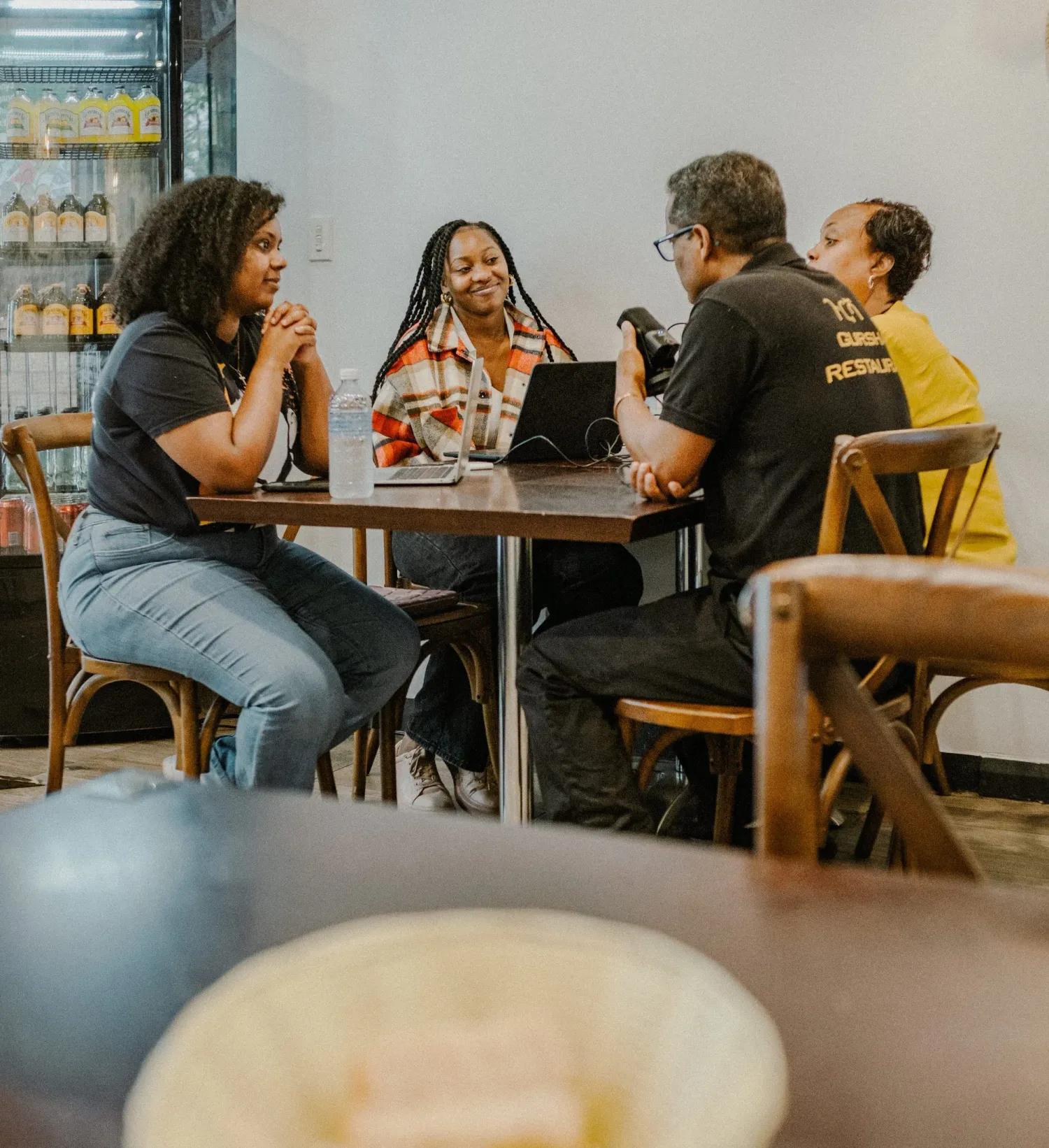 Four people having a lively conversation around a table in a bright modern cafe setting.