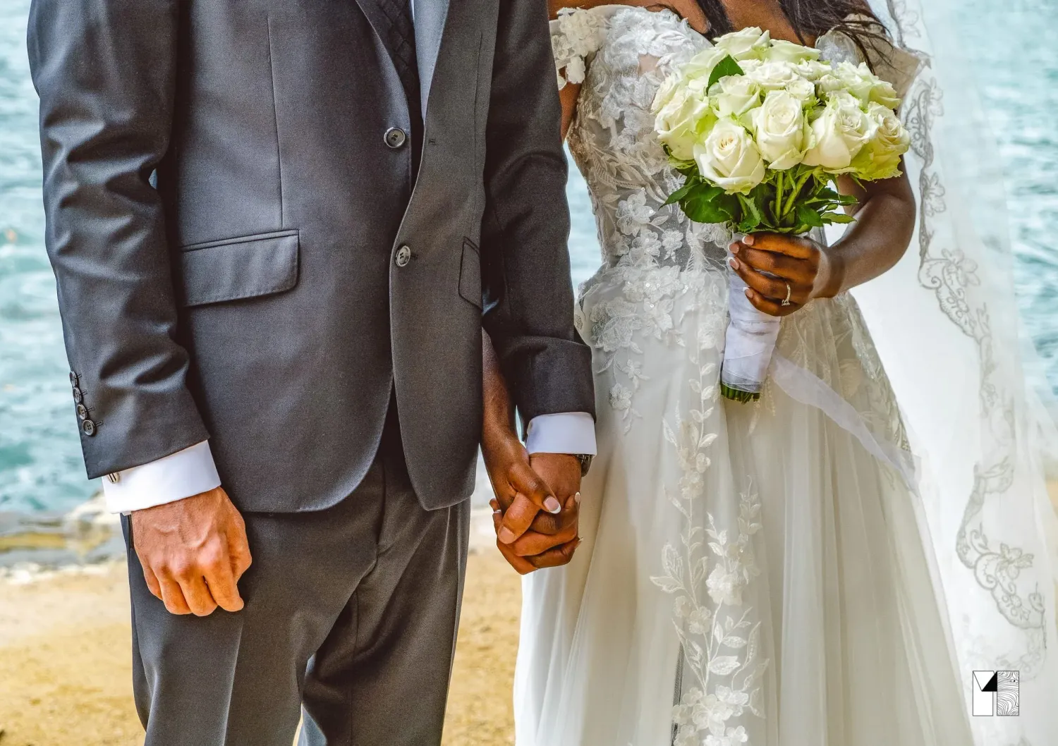 Newlyweds hold hands, bride carries white rose bouquet in elegant lace wedding gown.