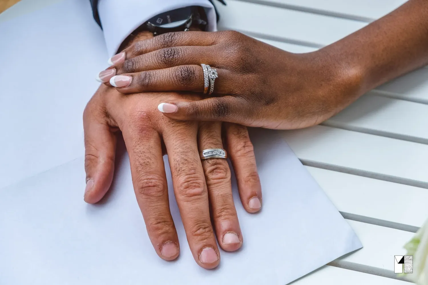 Close-up of newlywed couple's hands showing wedding rings on a white surface.