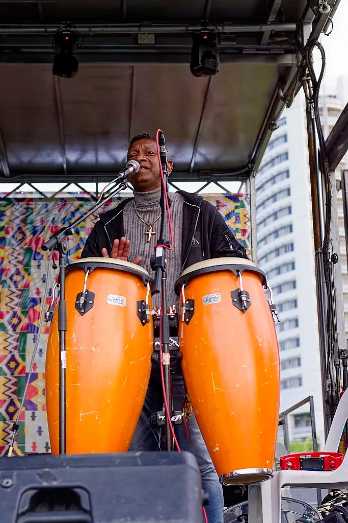 Man playing orange conga drums on stage at an outdoor African music festival.