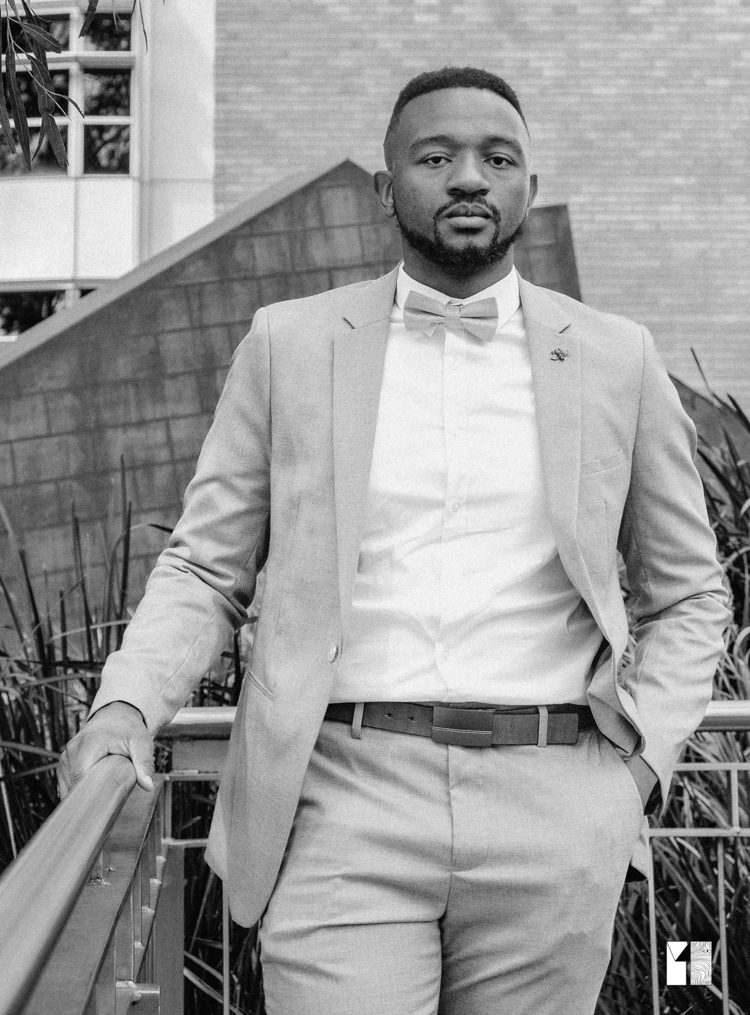 Black and white portrait of groom in gray suit and bow tie standing outdoors.