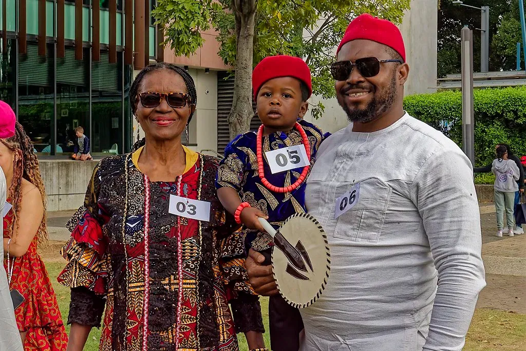 Family in traditional Nigerian Igbo attire posing together at a multicultural cultural festival outdoors.