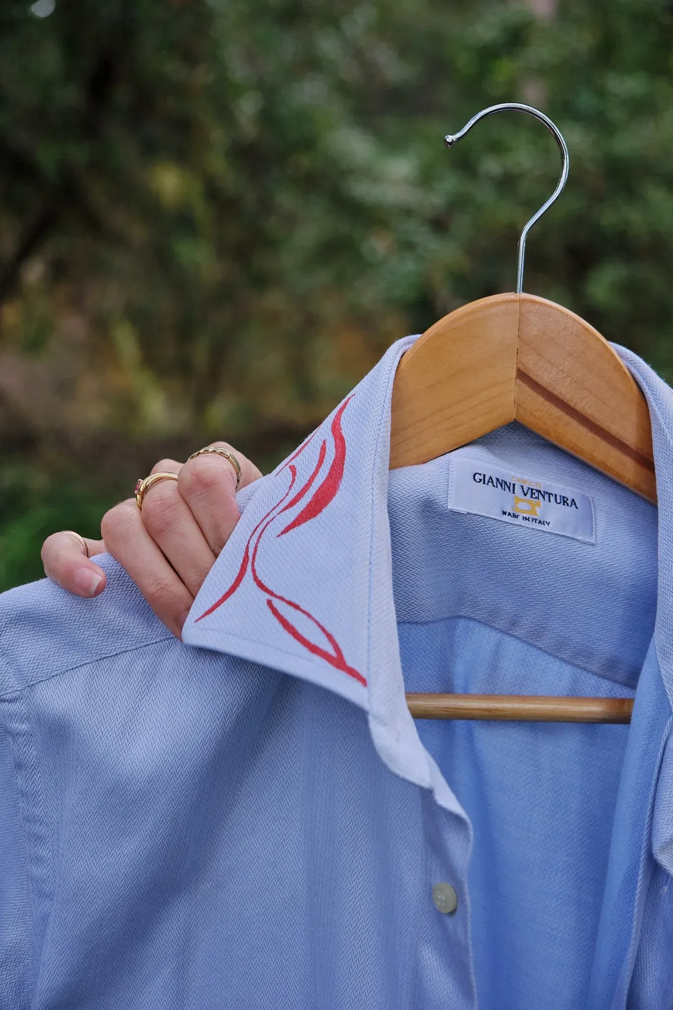 Light blue Gianni Ventura shirt on wooden hanger held by hand with rings.