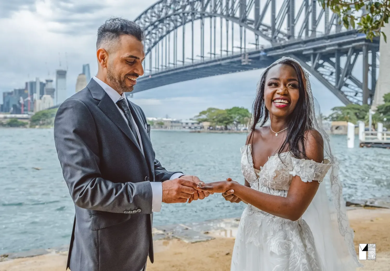 Interracial couple exchanging rings at Sydney Harbour Bridge waterfront wedding ceremony.