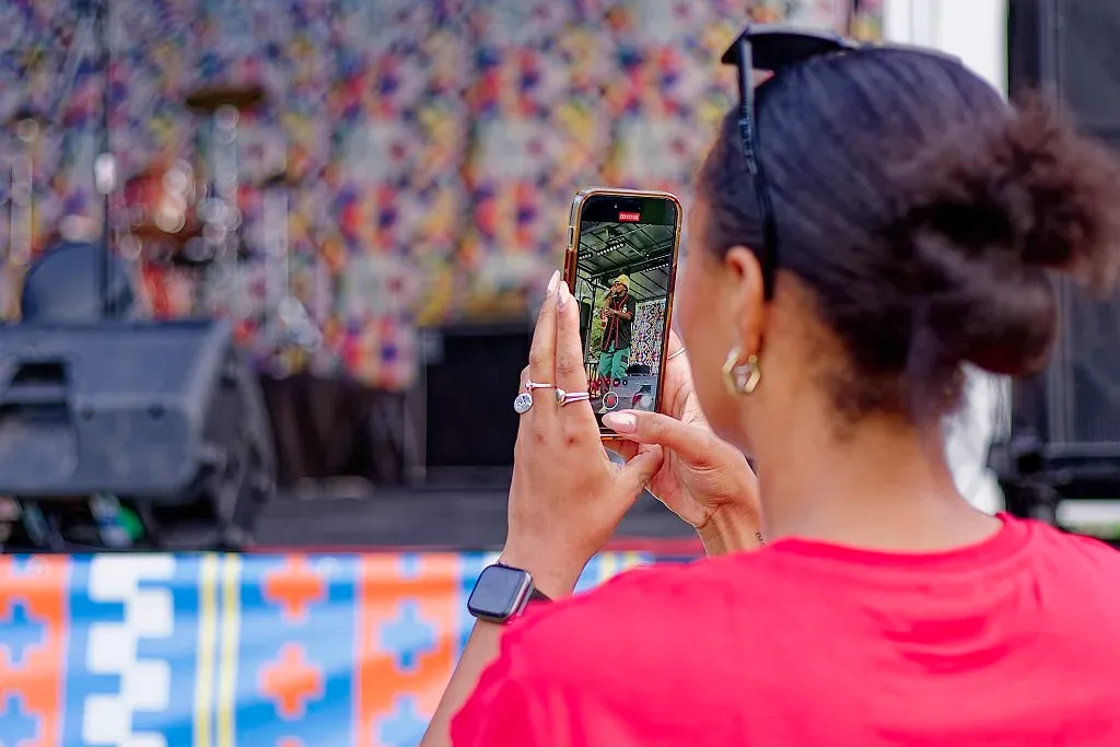 Woman in red shirt photographing a cultural festival performance on smartphone.