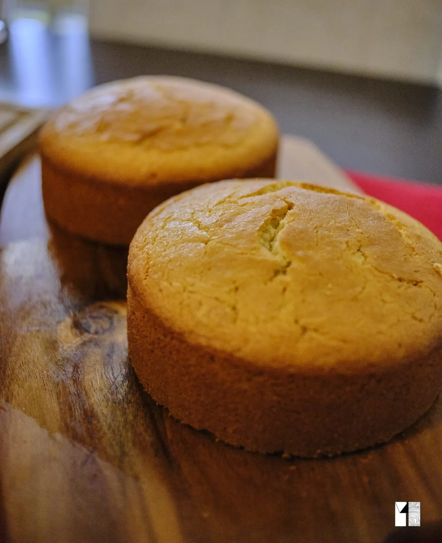 Two golden-brown round sponge cake layers cooling on a rustic wooden cutting board.