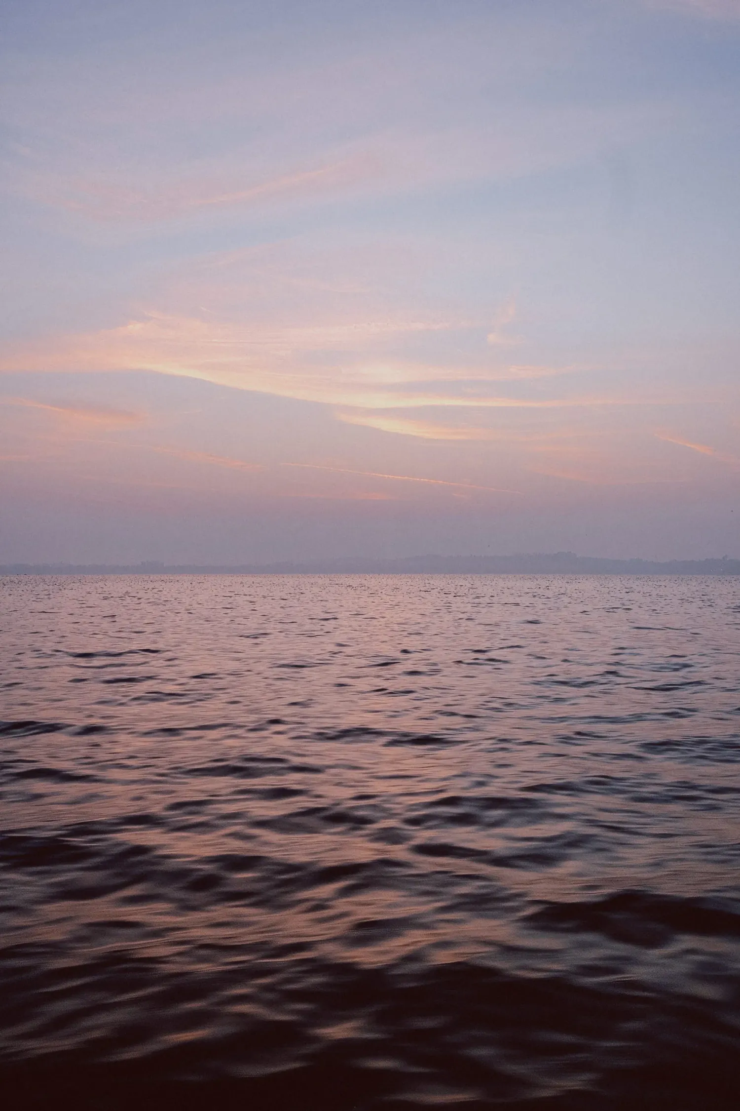 Serene sunset over calm ocean waters with soft pink and purple hues reflecting on gentle waves.
