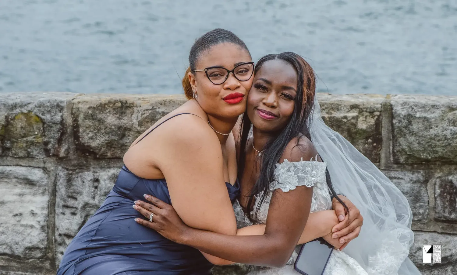 Bridesmaid and bride sharing a warm embrace near the waterfront.