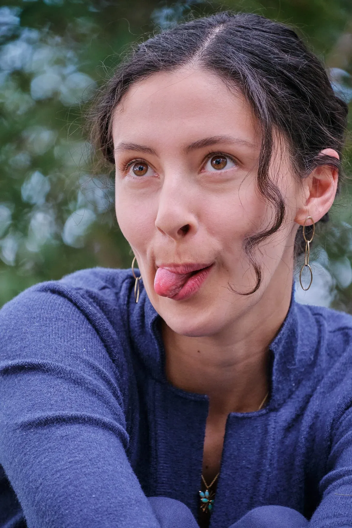 Close-up portrait of dark-haired woman sticking out tongue playfully outdoors.