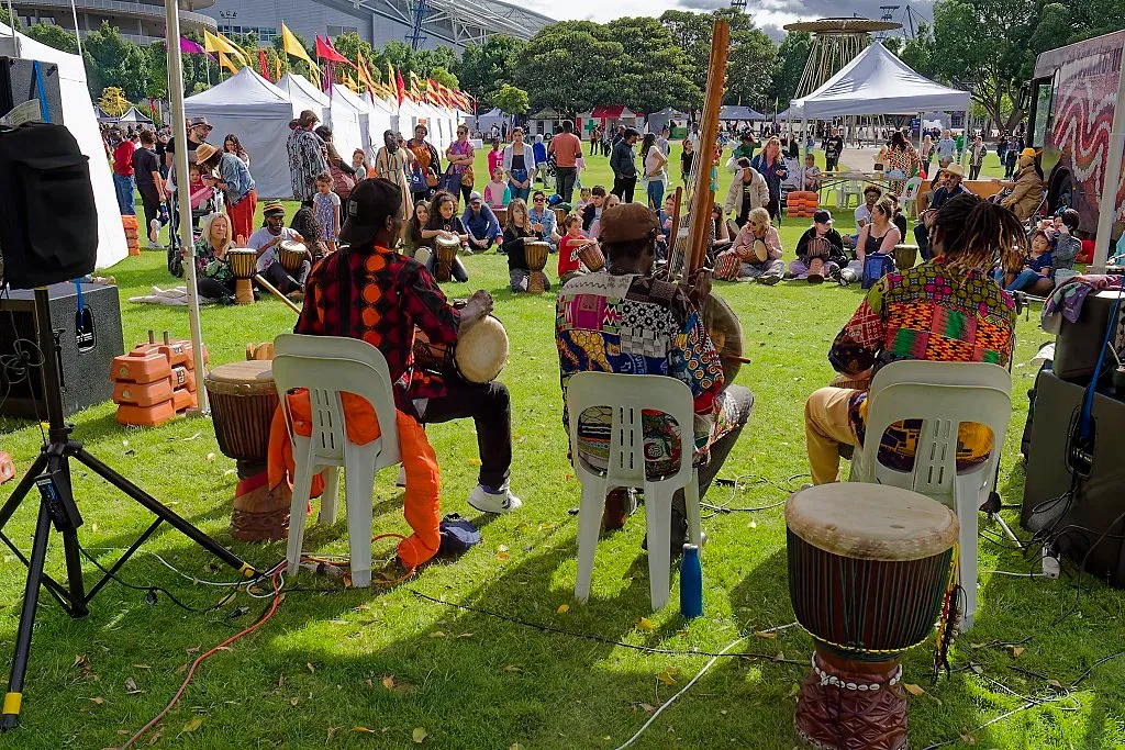 Musicians playing djembe drums on grass at vibrant outdoor African cultural festival.