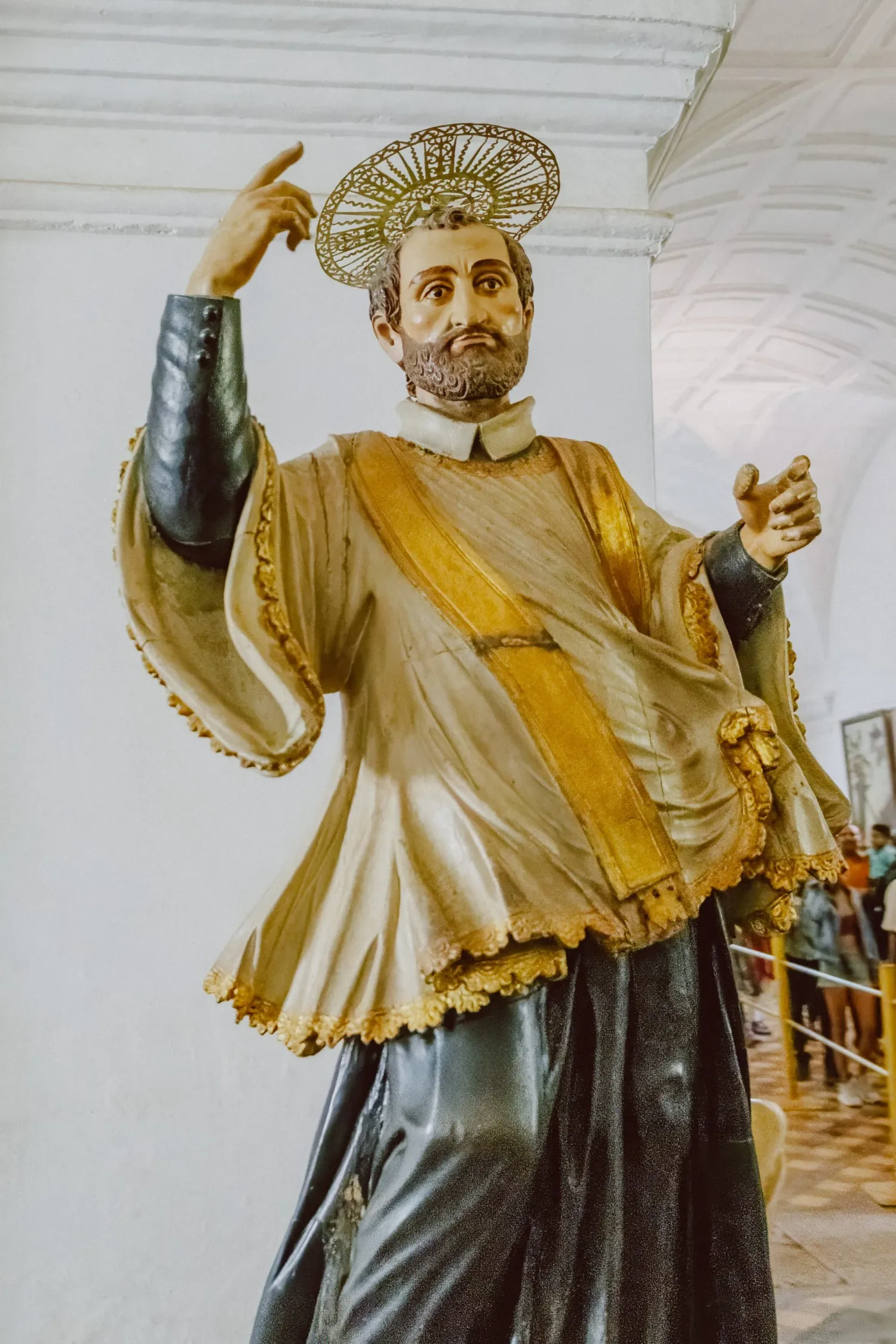 Ornate golden statue of a Catholic saint with halo gesturing in a white colonial church interior.