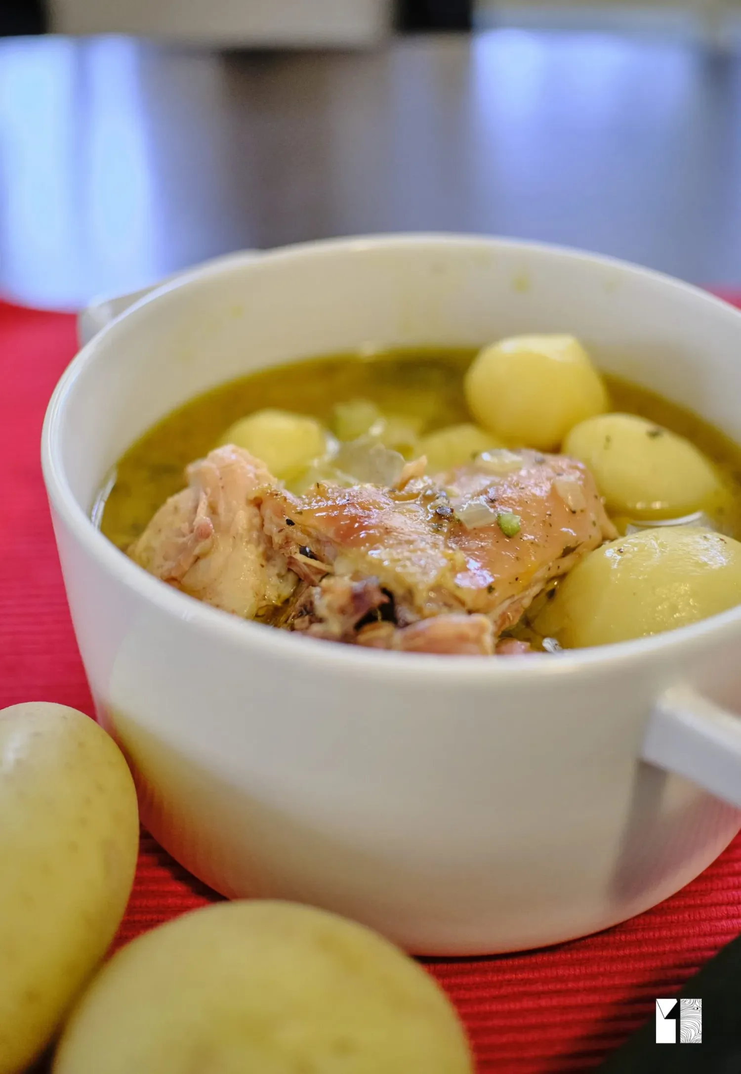 Chicken stew with potatoes served in a white bowl on a red surface.