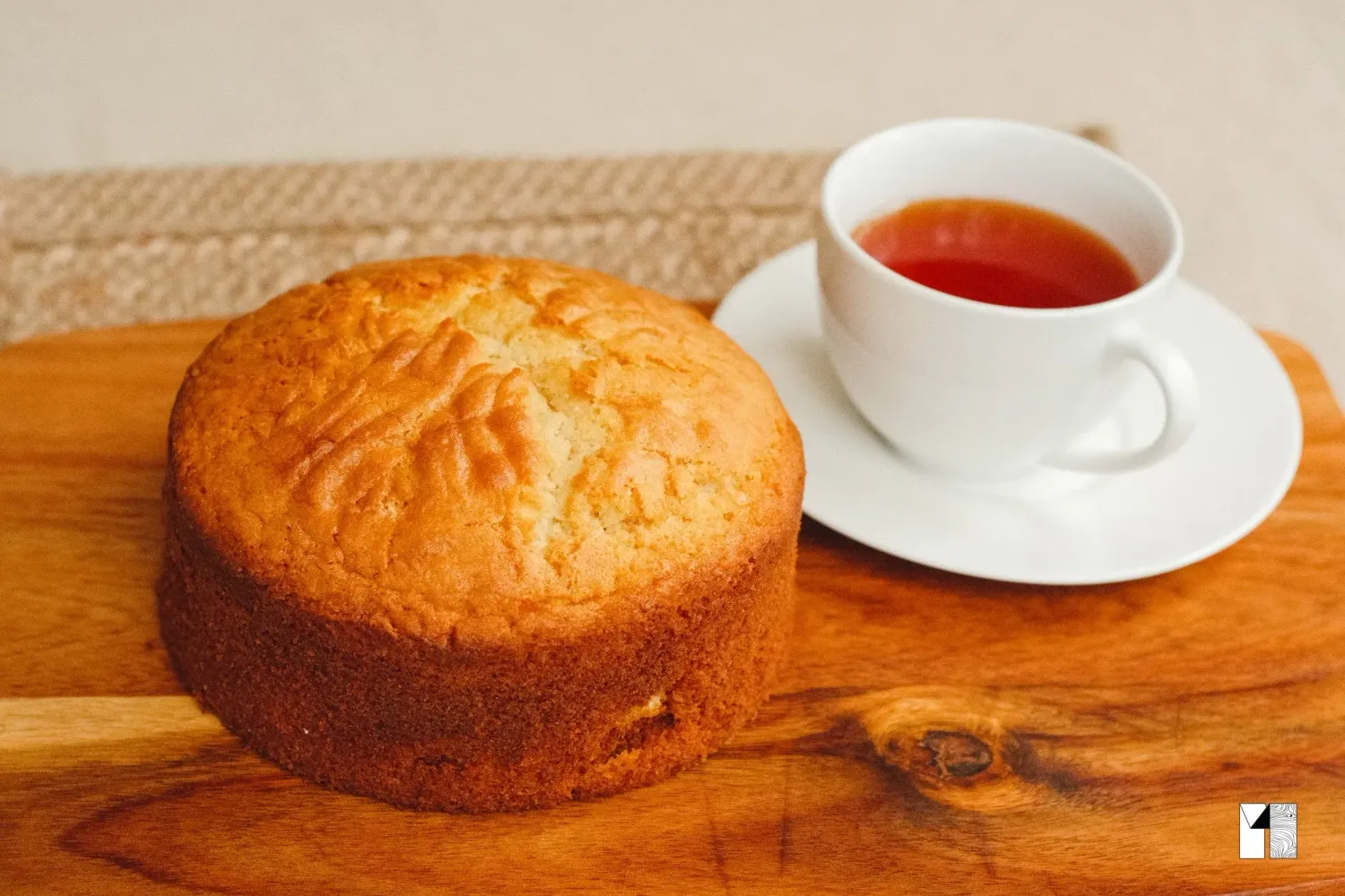 Golden sponge cake on a wooden board served alongside a cup of hot tea on a saucer.