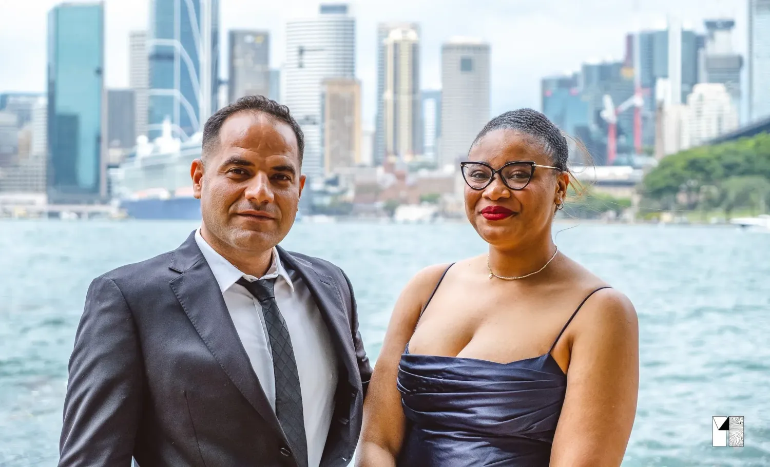 Elegant couple posing with Sydney city skyline and harbour in background.