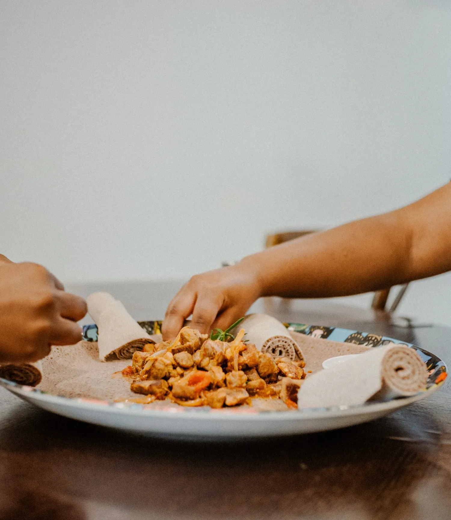 Two people sharing a traditional Ethiopian injera meal with spiced meat and vegetable toppings.