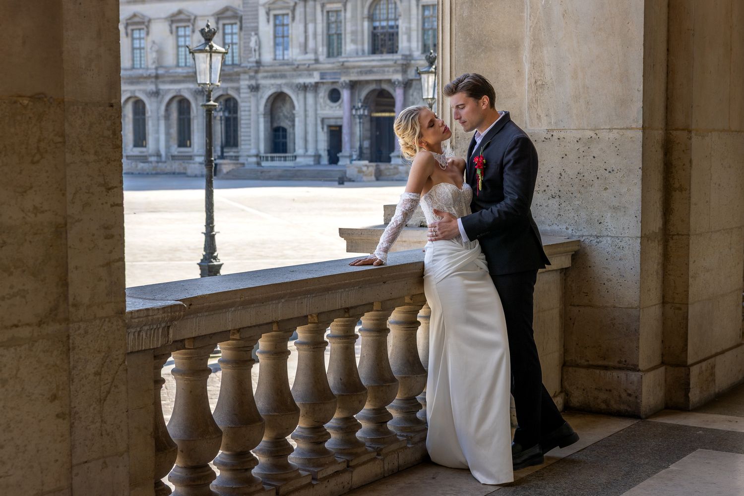A bride and groom share a romantic embrace on a balcony with classical architecture.