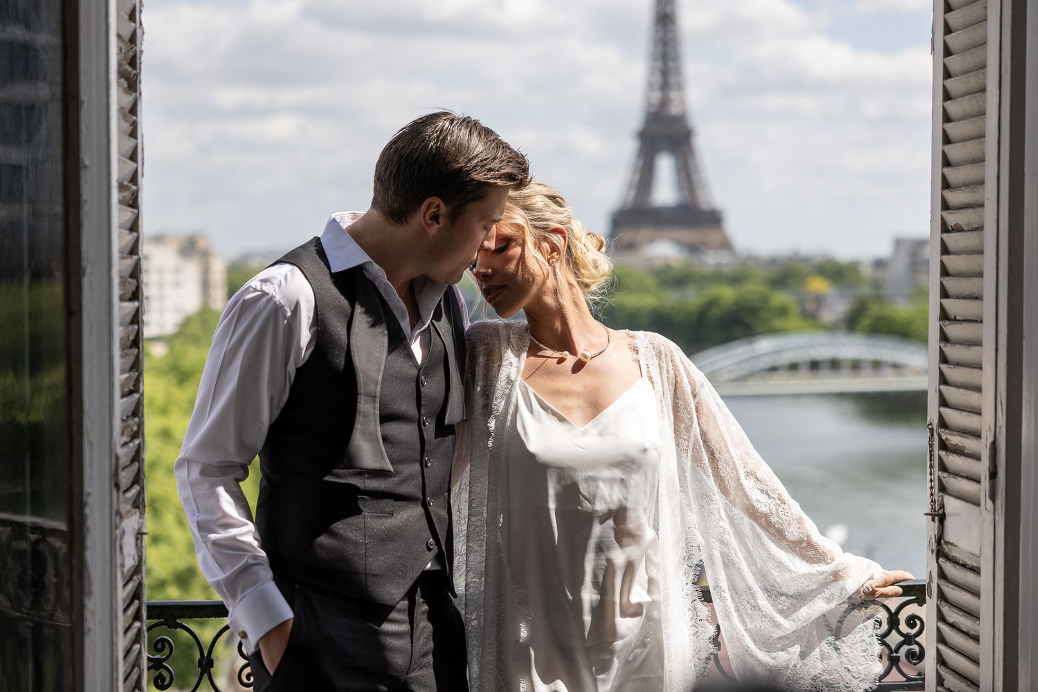 Bride and groom sharing intimate moment on balcony with Eiffel Tower in background.