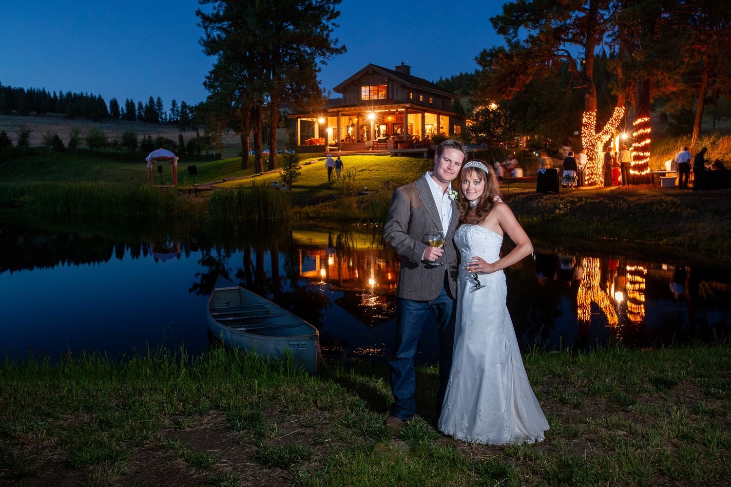 Bride and groom posing elegantly by a pond at night with a beautifully lit house in background.