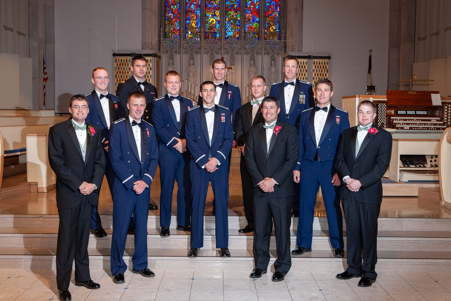 Group of men in military dress blues and tuxedos pose together inside a church for a wedding photo.