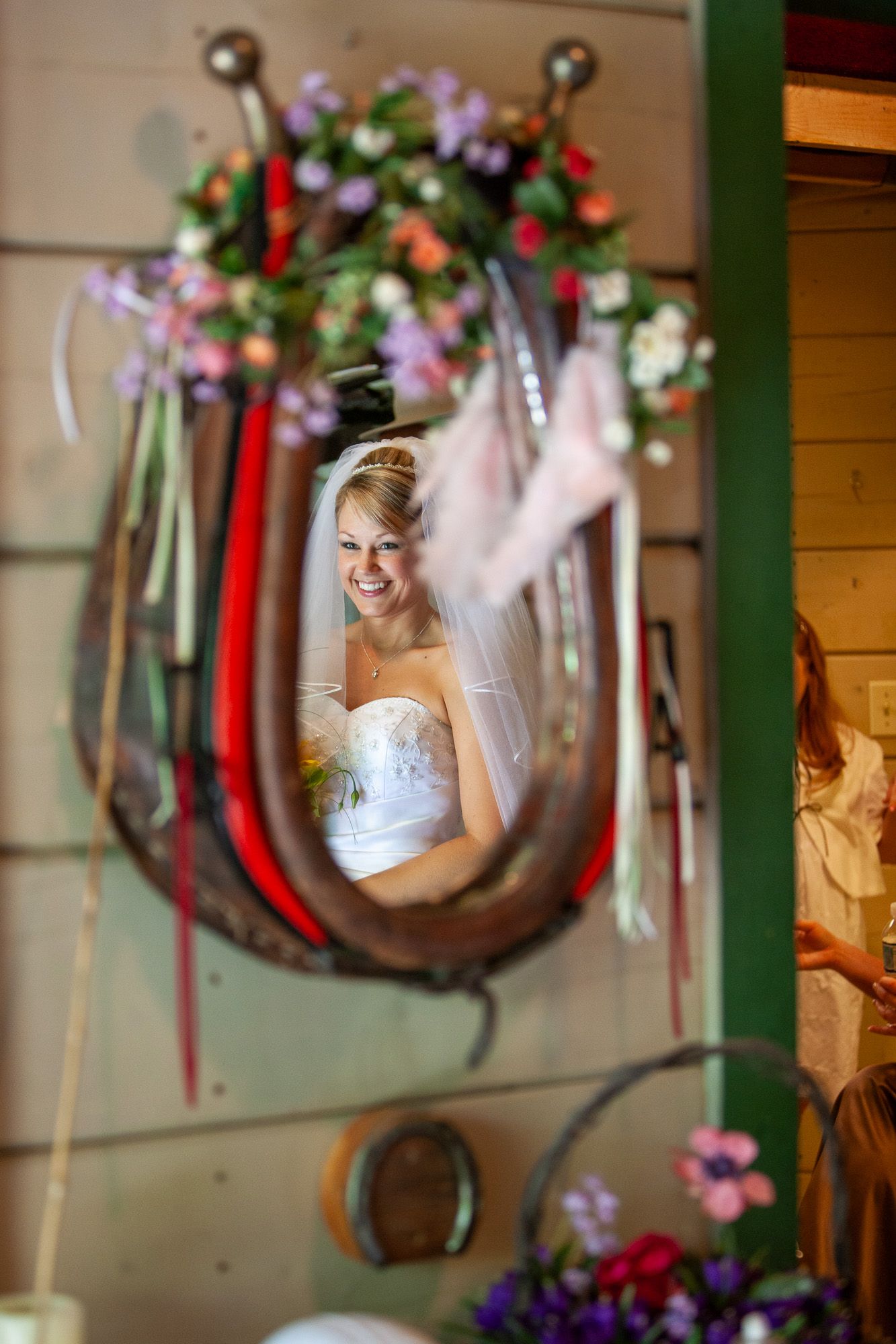 Bride smiling in reflection of horseshoe-shaped mirror decorated with flowers and ribbons.