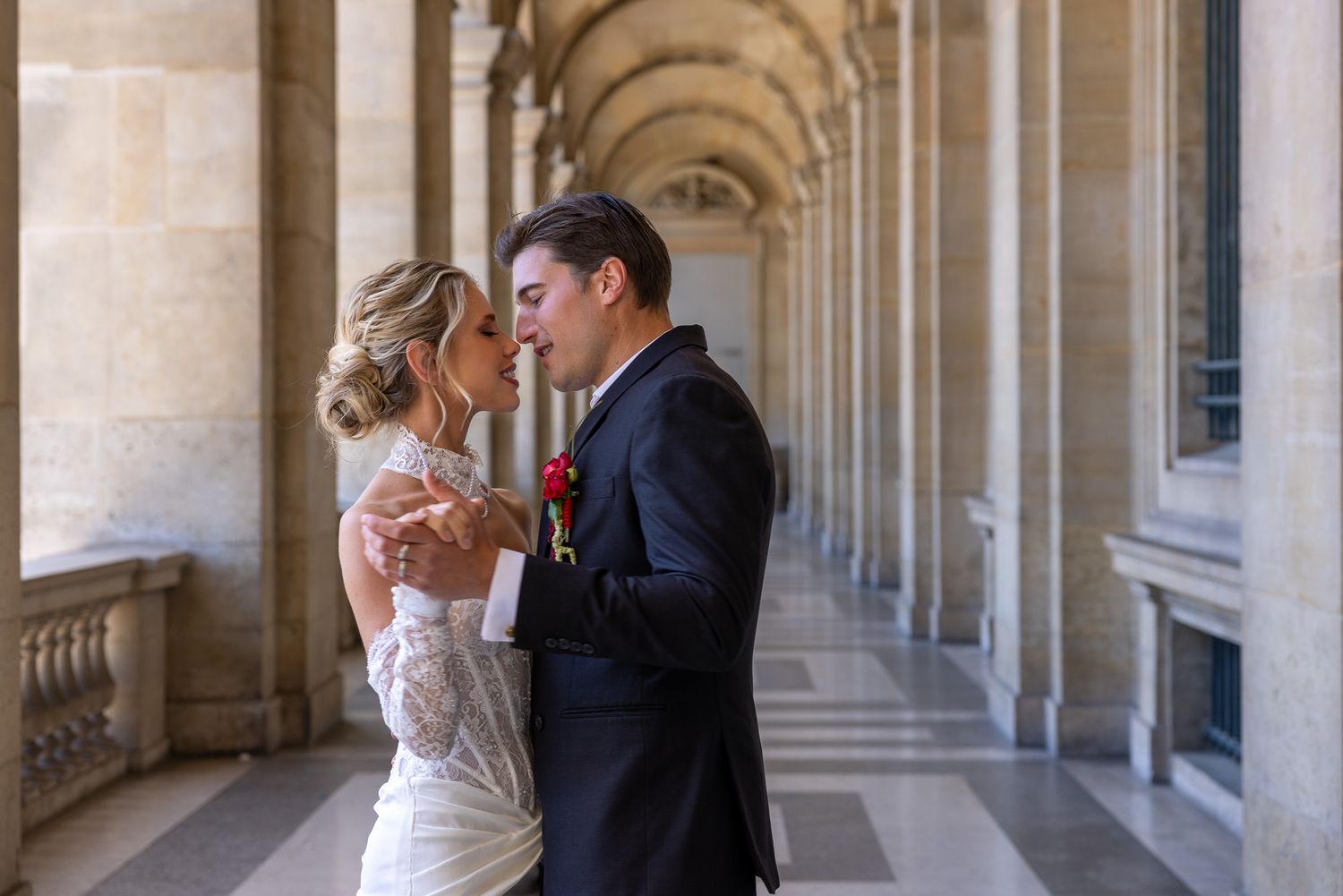 A bride and groom share an intimate moment in an elegant arched corridor.