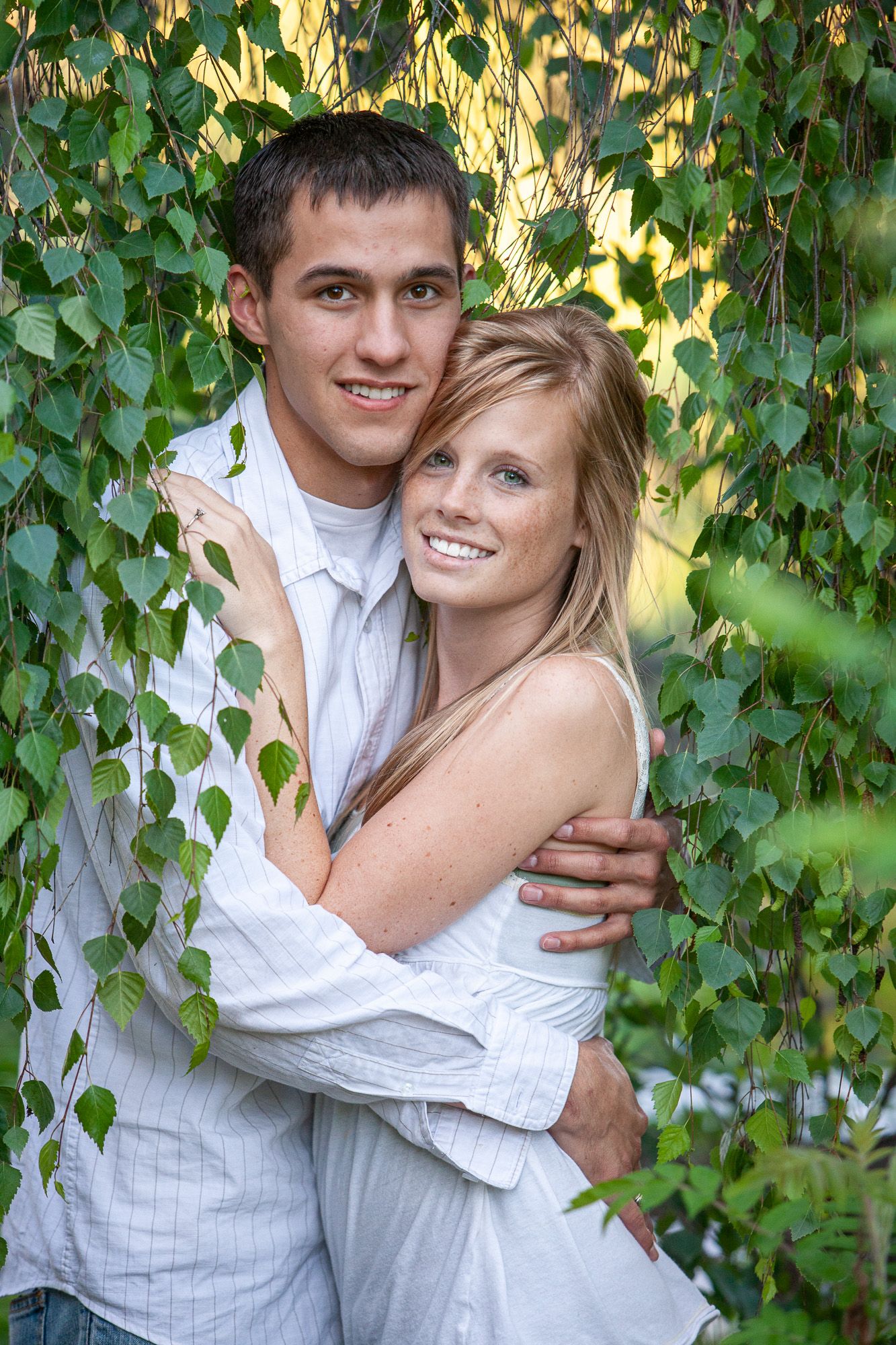 Happy young couple hugging and smiling together framed by hanging green ivy leaves outdoors.
