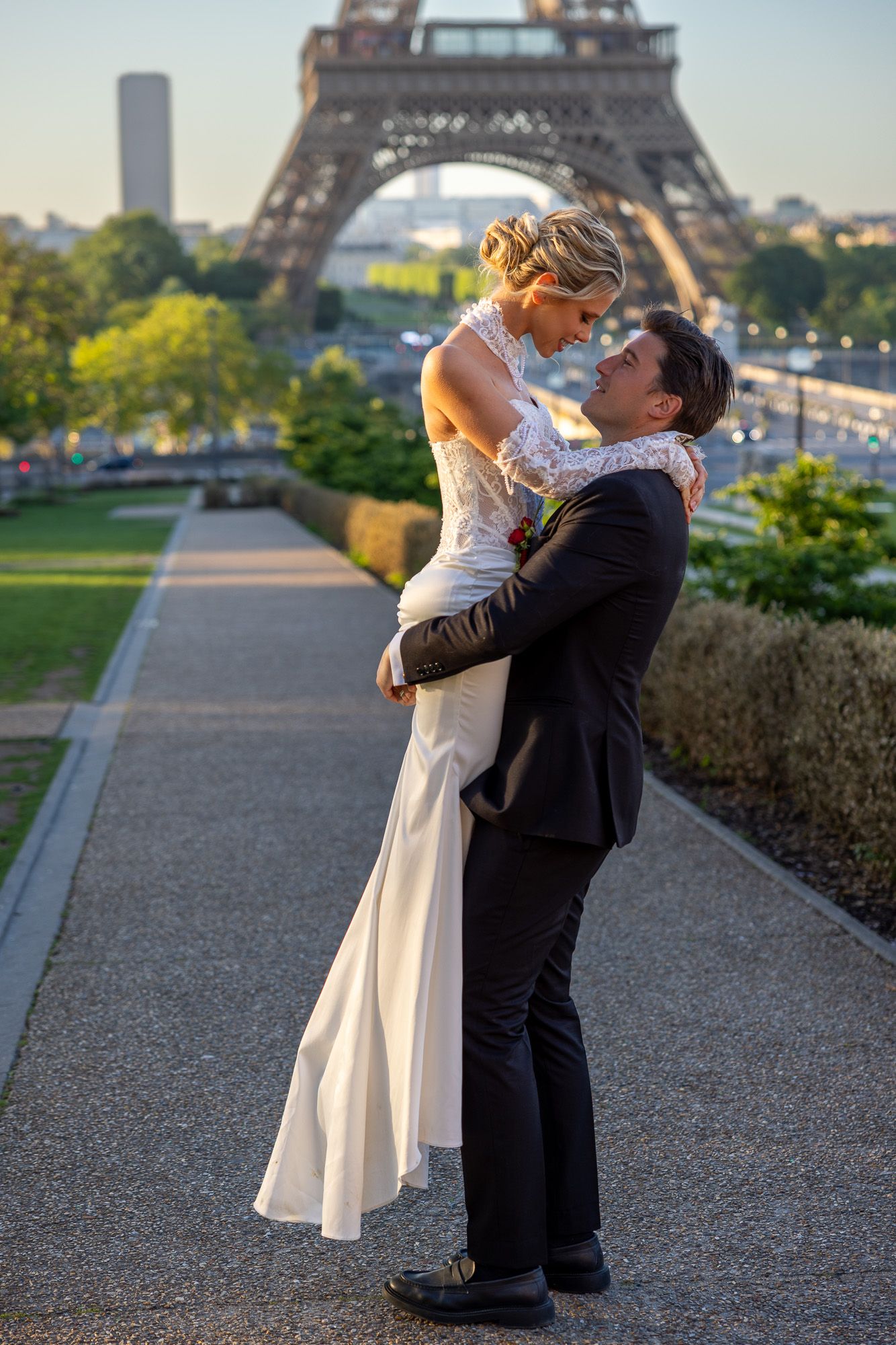 Groom lifts bride joyfully on a Paris pathway with the Eiffel Tower at sunset.