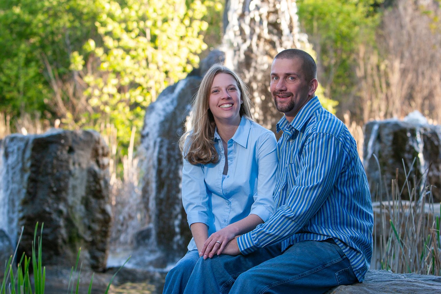 Smiling couple sitting together outdoors near a scenic waterfall backdrop.