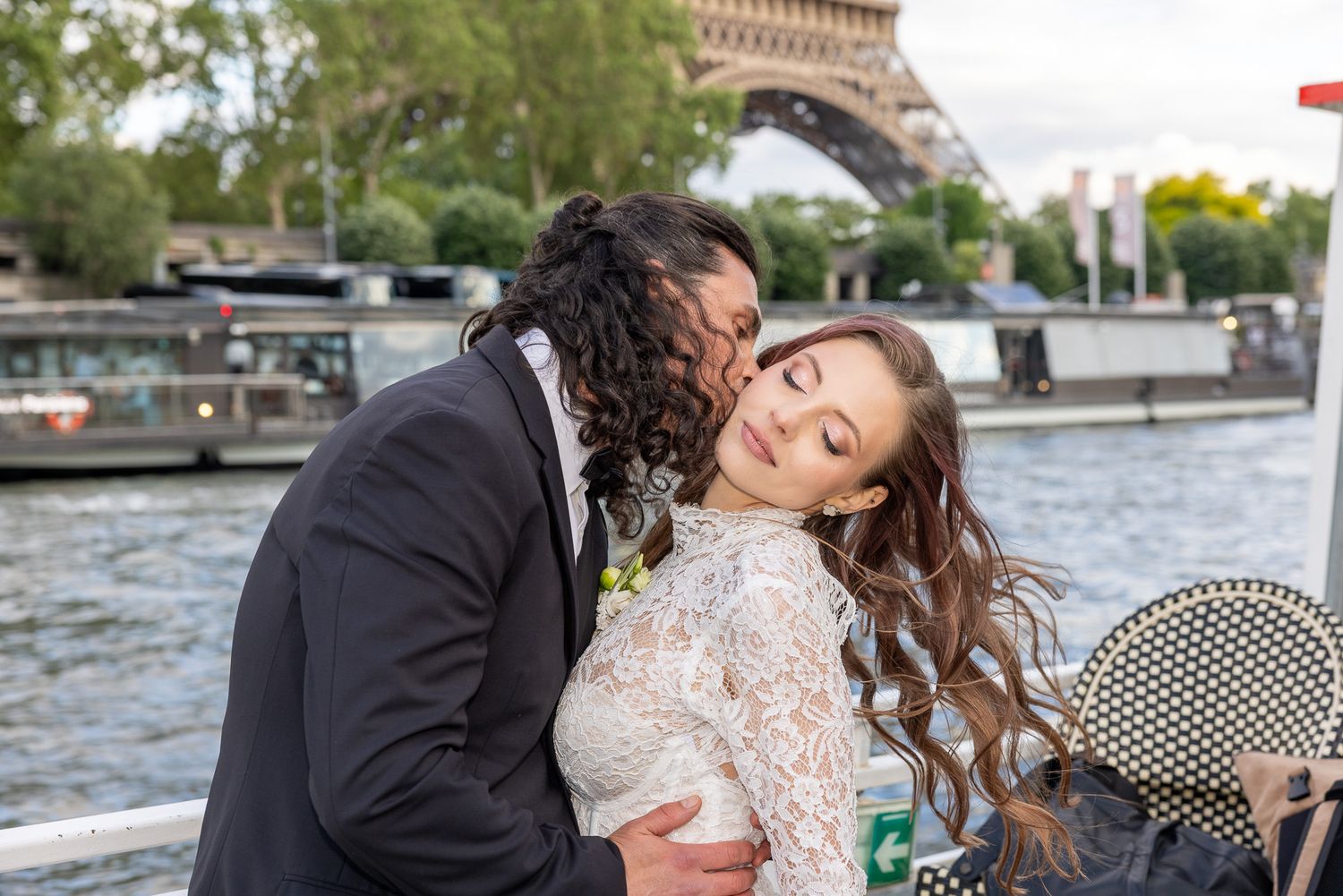 Groom kissing bride on cheek as she smiles blissfully near the Eiffel Tower.