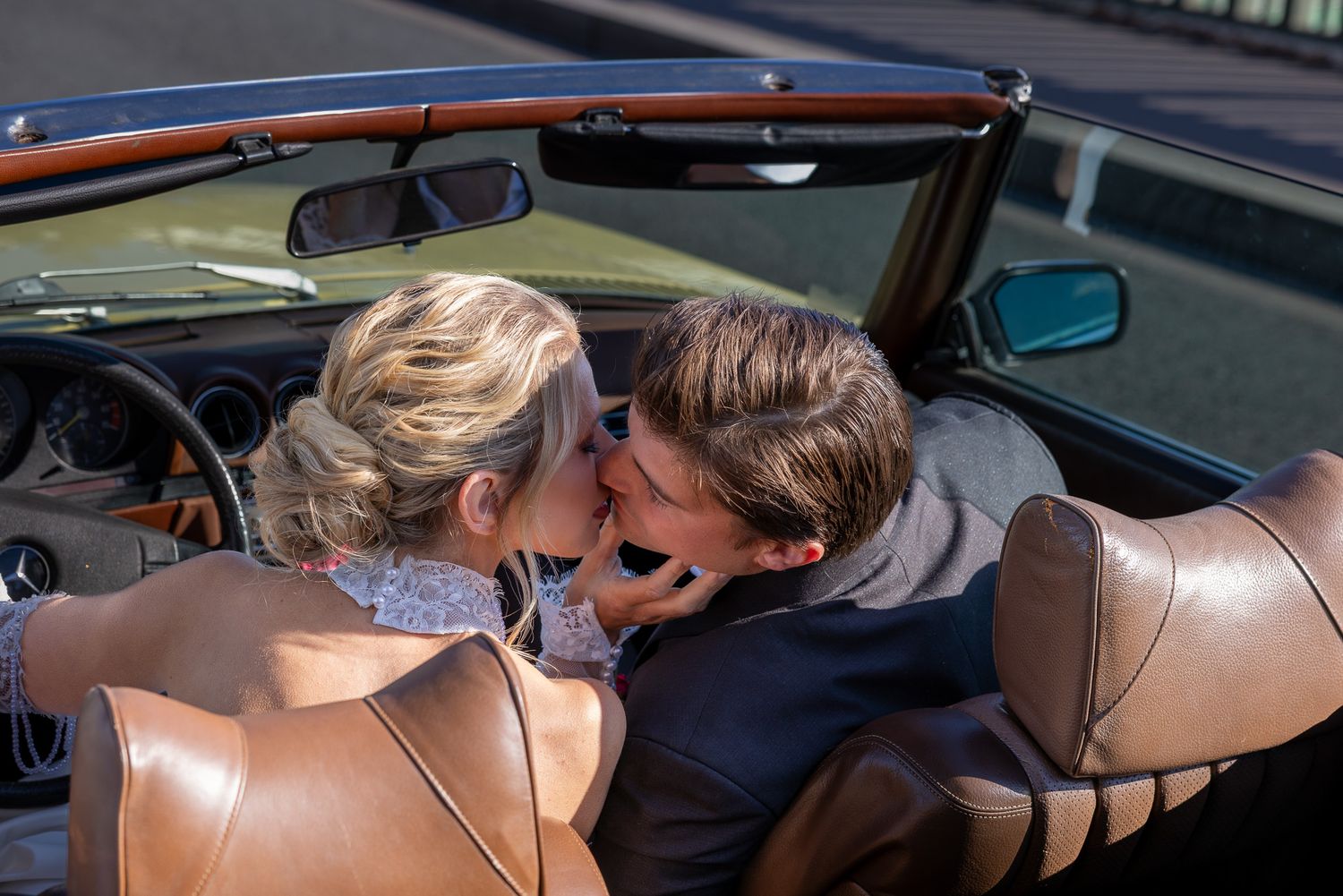 A couple shares a romantic kiss in a classic convertible car on a sunny day.