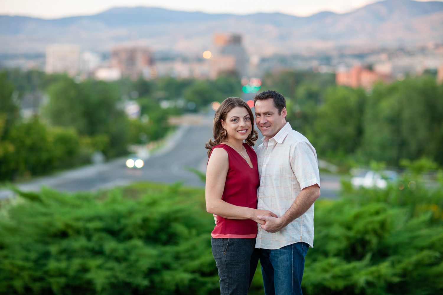 Happy couple embracing with a panoramic city skyline and mountain backdrop during an engagement session.