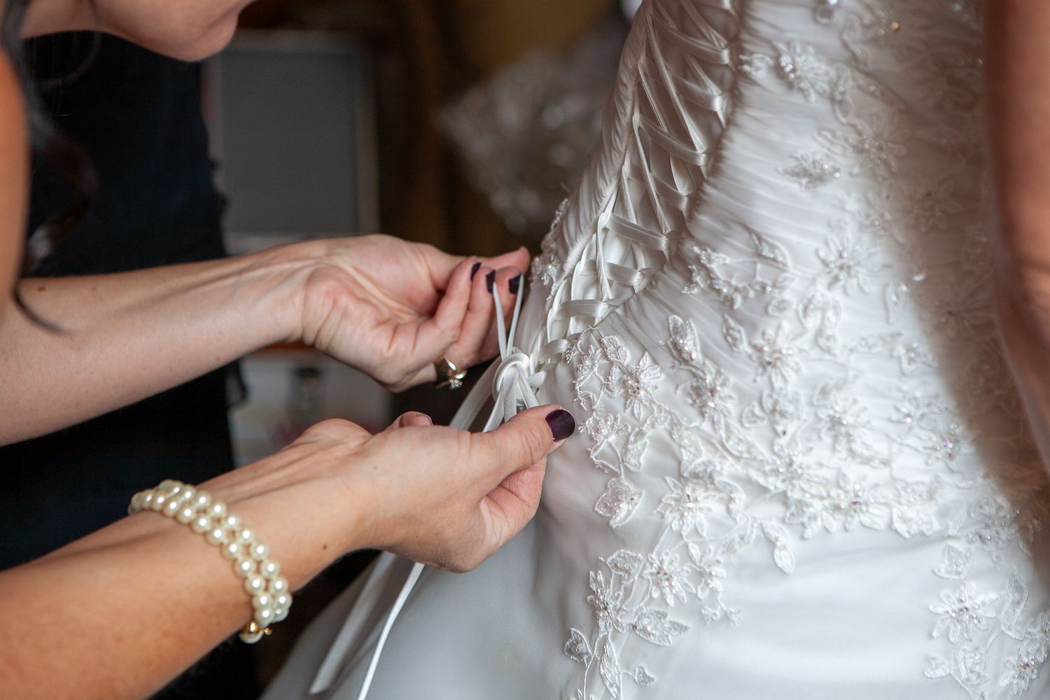 Bridesmaid lacing up back of brides intricate white lace wedding gown.
