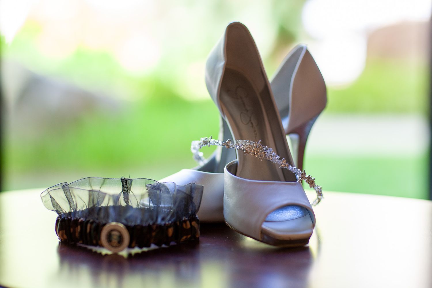 White satin wedding heels with crystal bracelet and decorative garter on wooden table.