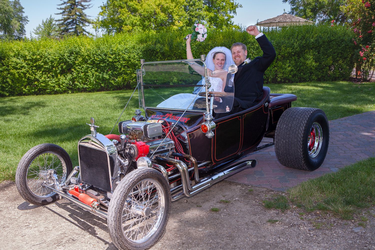 Happy bride and groom celebrate in a vintage black hot rod custom car on their wedding day.