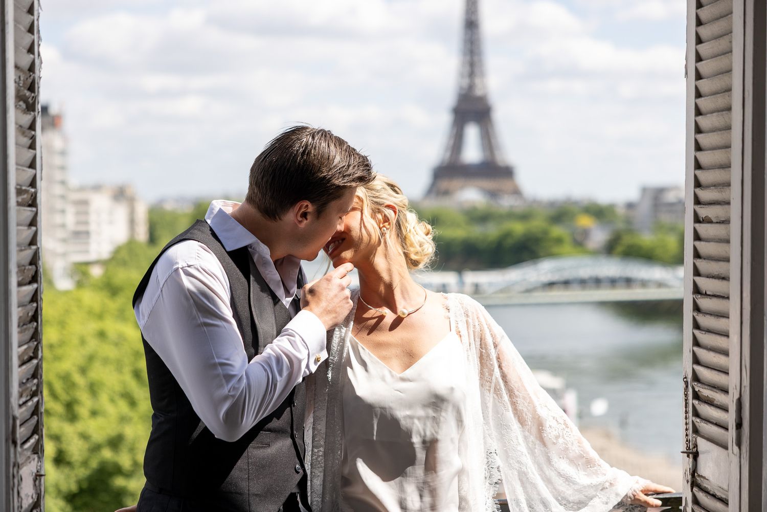 Romantic couple sharing tender moment on Parisian balcony with Eiffel Tower in background.