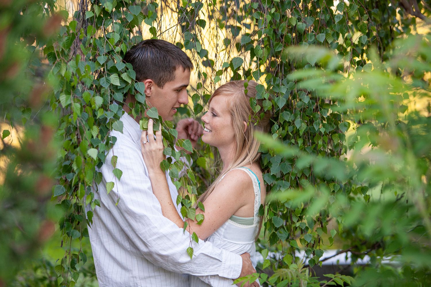 Romantic couple embracing and smiling at each other surrounded by lush green ivy vines outdoors.