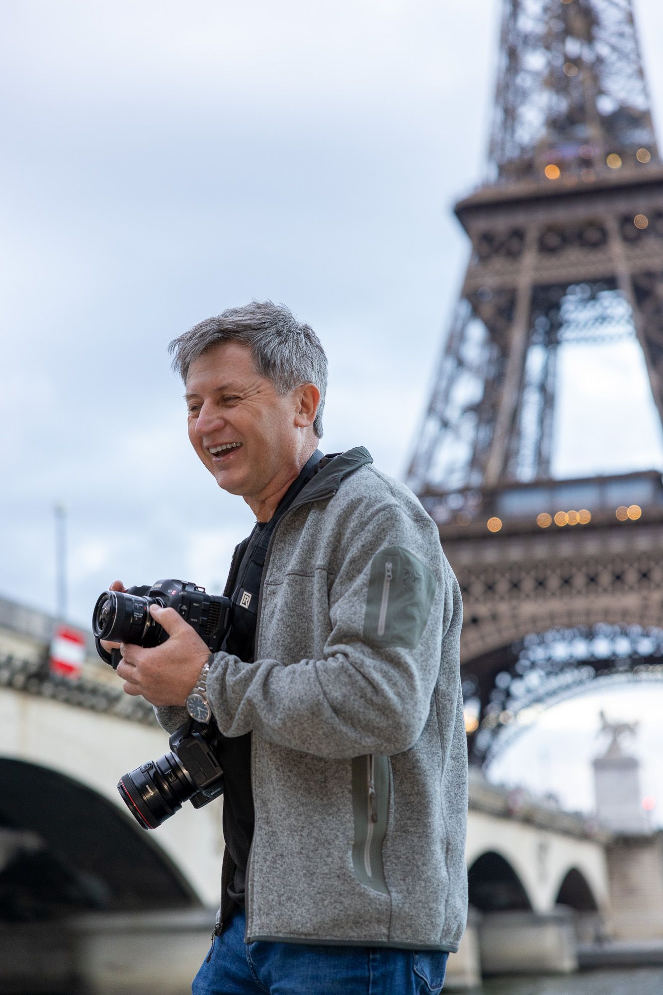 Smiling male photographer holding camera near the illuminated Eiffel Tower in Paris.