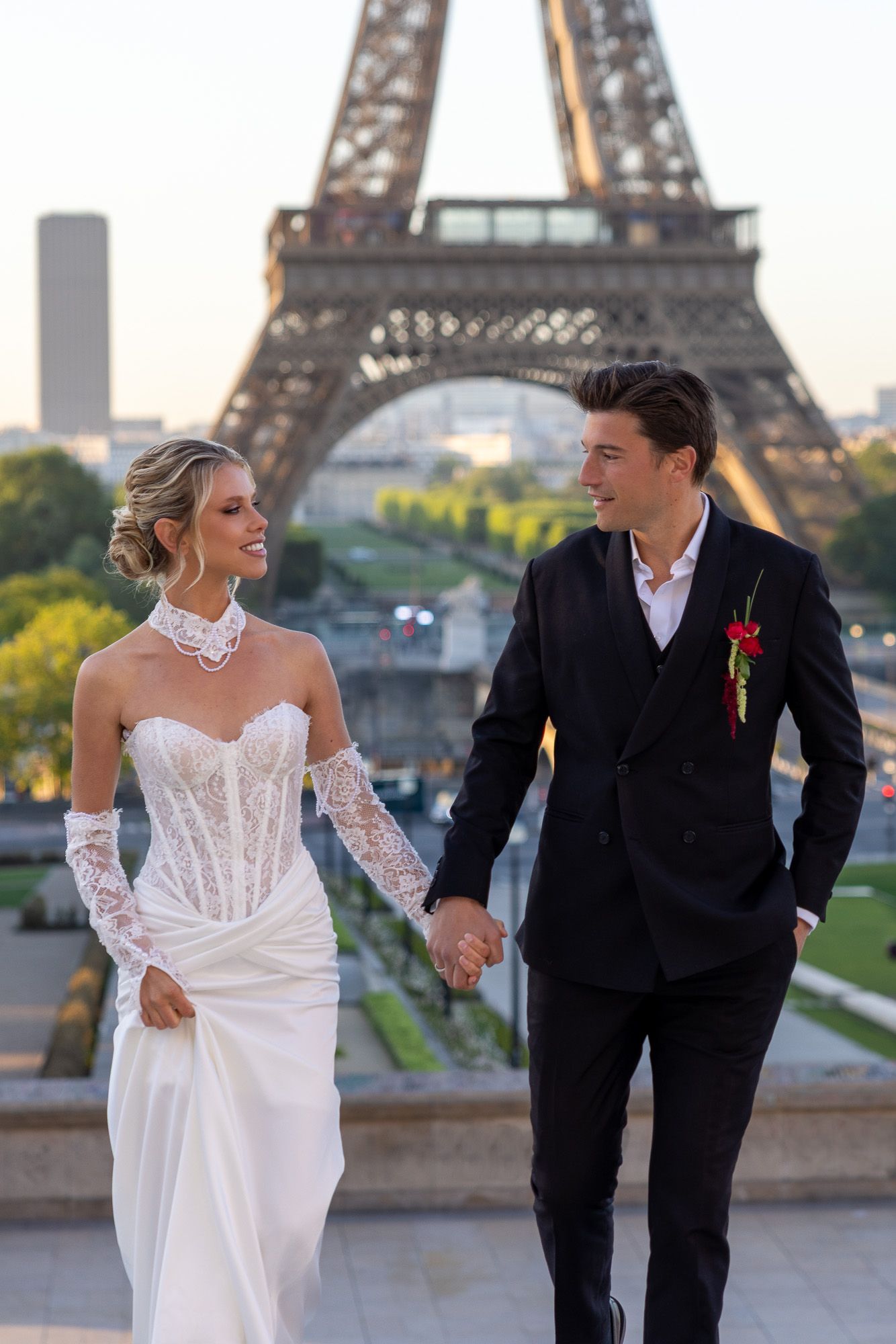Smiling newlyweds walk hand in hand with the Eiffel Tower at golden hour.