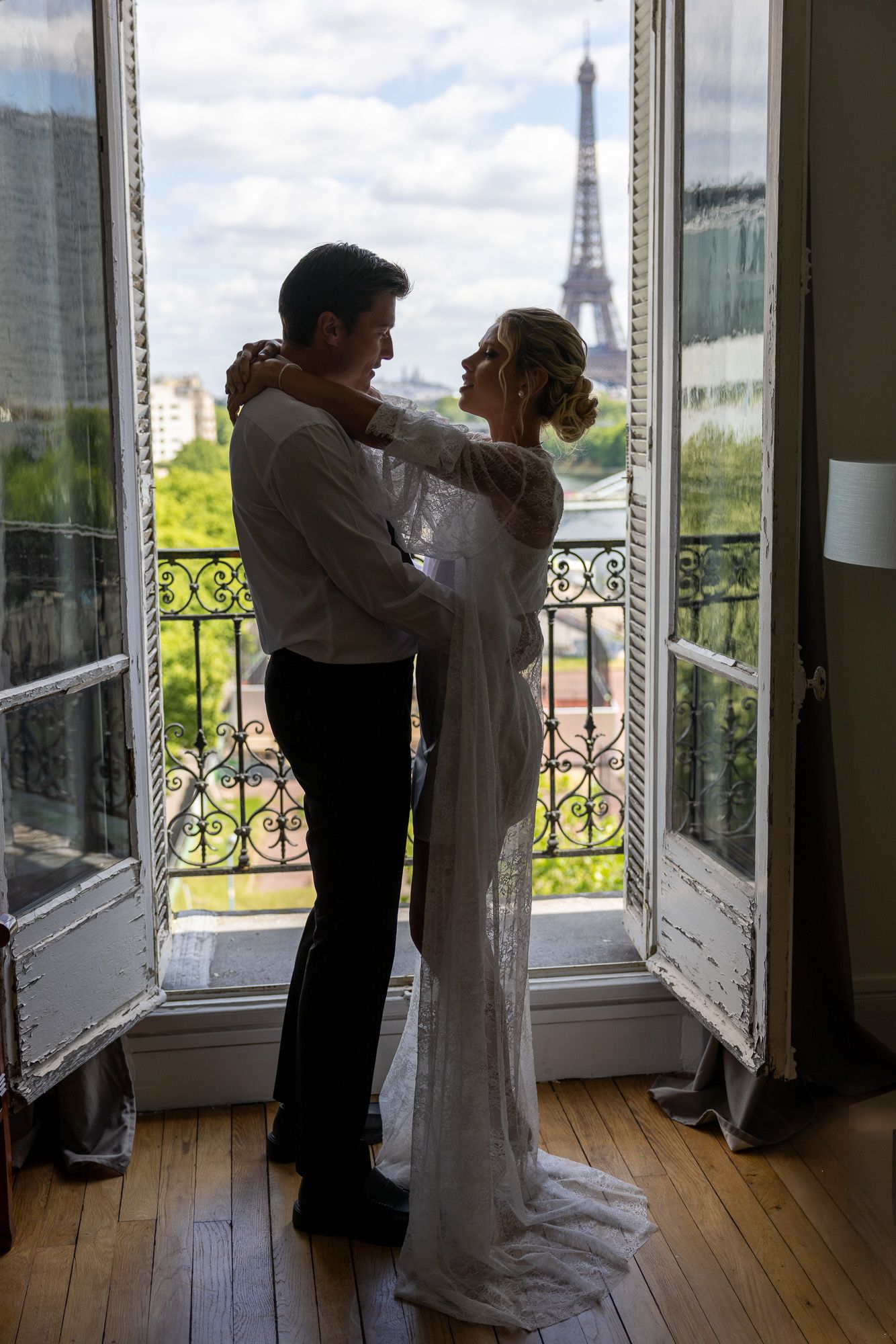 Bride and groom dance together by open French doors with Eiffel Tower view.