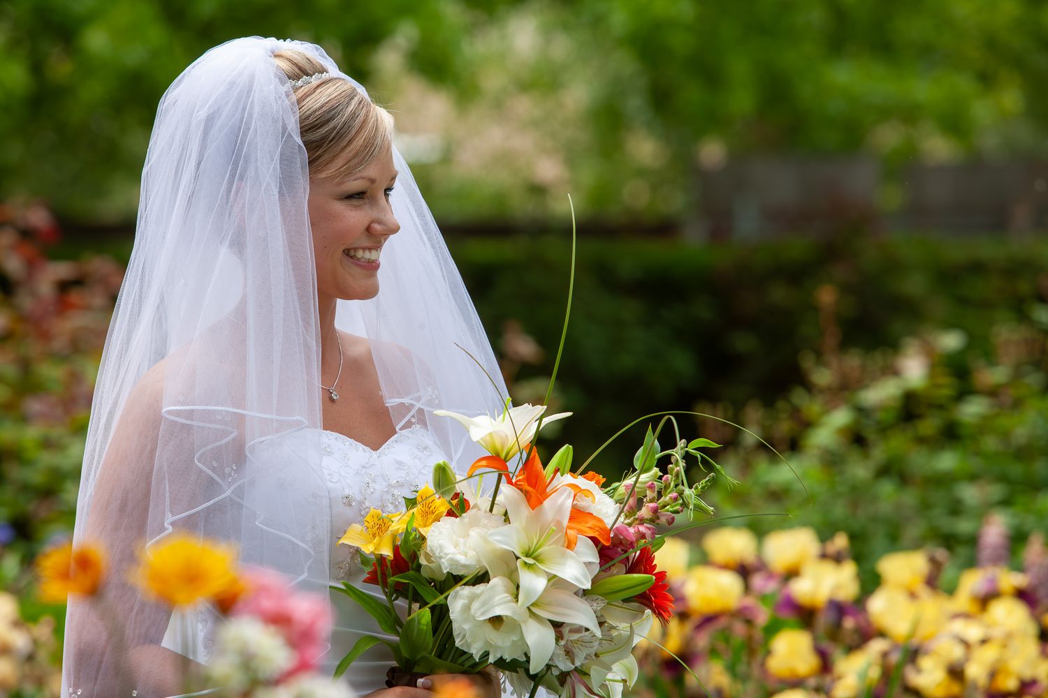 Beautiful bride wearing a veil and holding a colorful bouquet of flowers in a garden setting.
