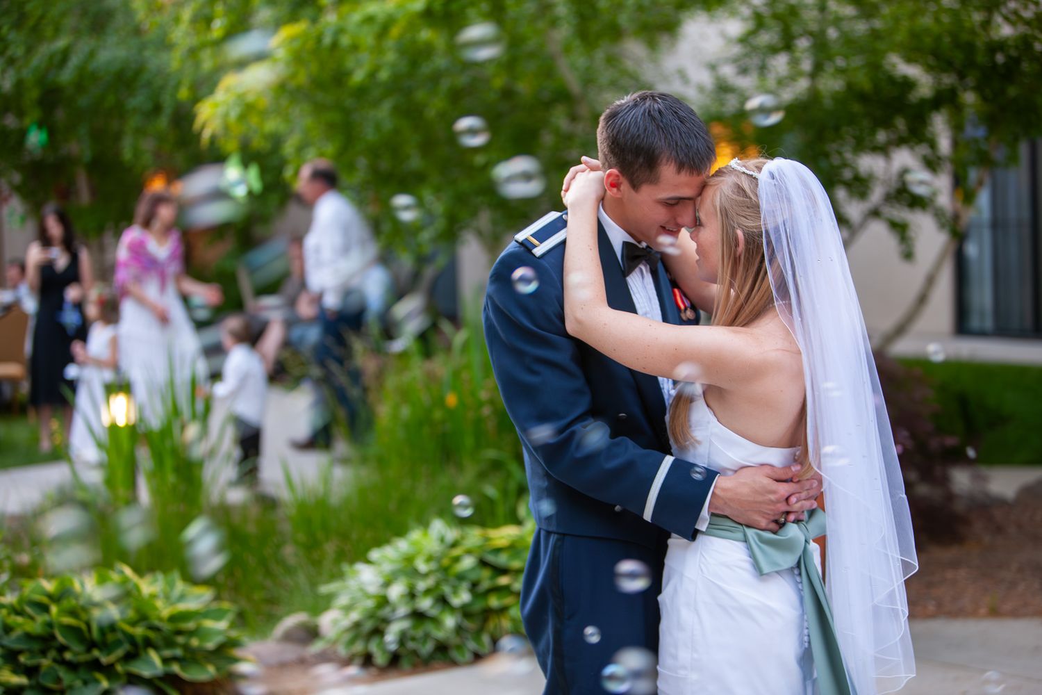 Bride and groom sharing a tender kiss outdoors surrounded by floating soap bubbles at their wedding.