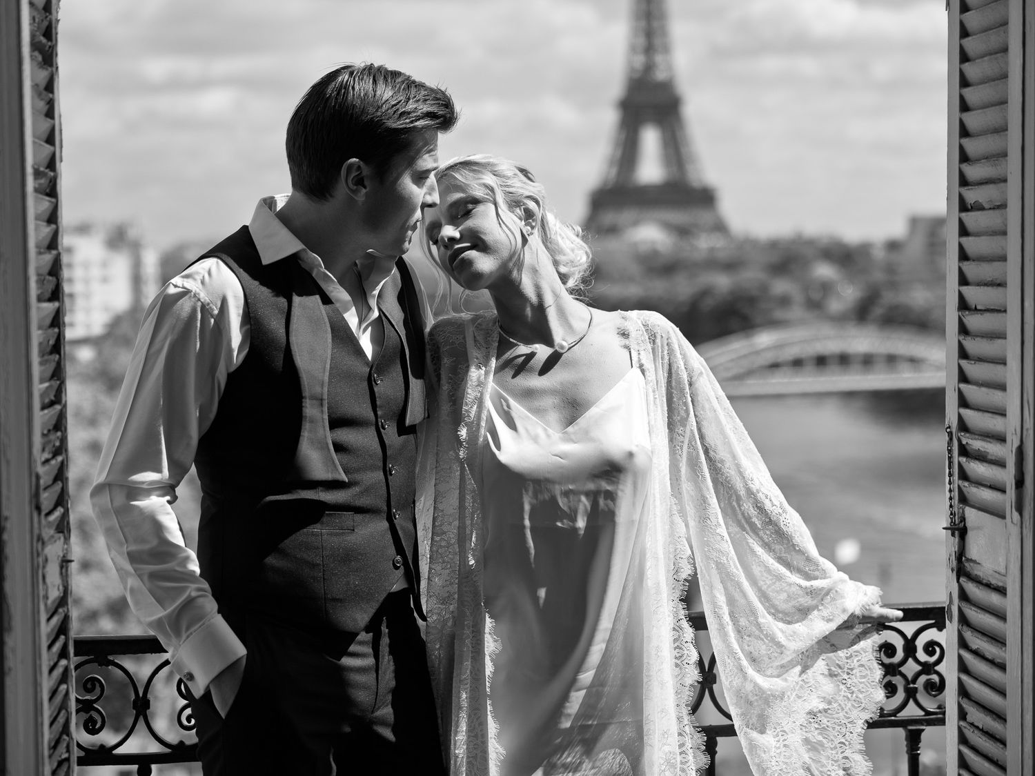 Bride and groom sharing romantic moment on Paris balcony with Eiffel Tower view.