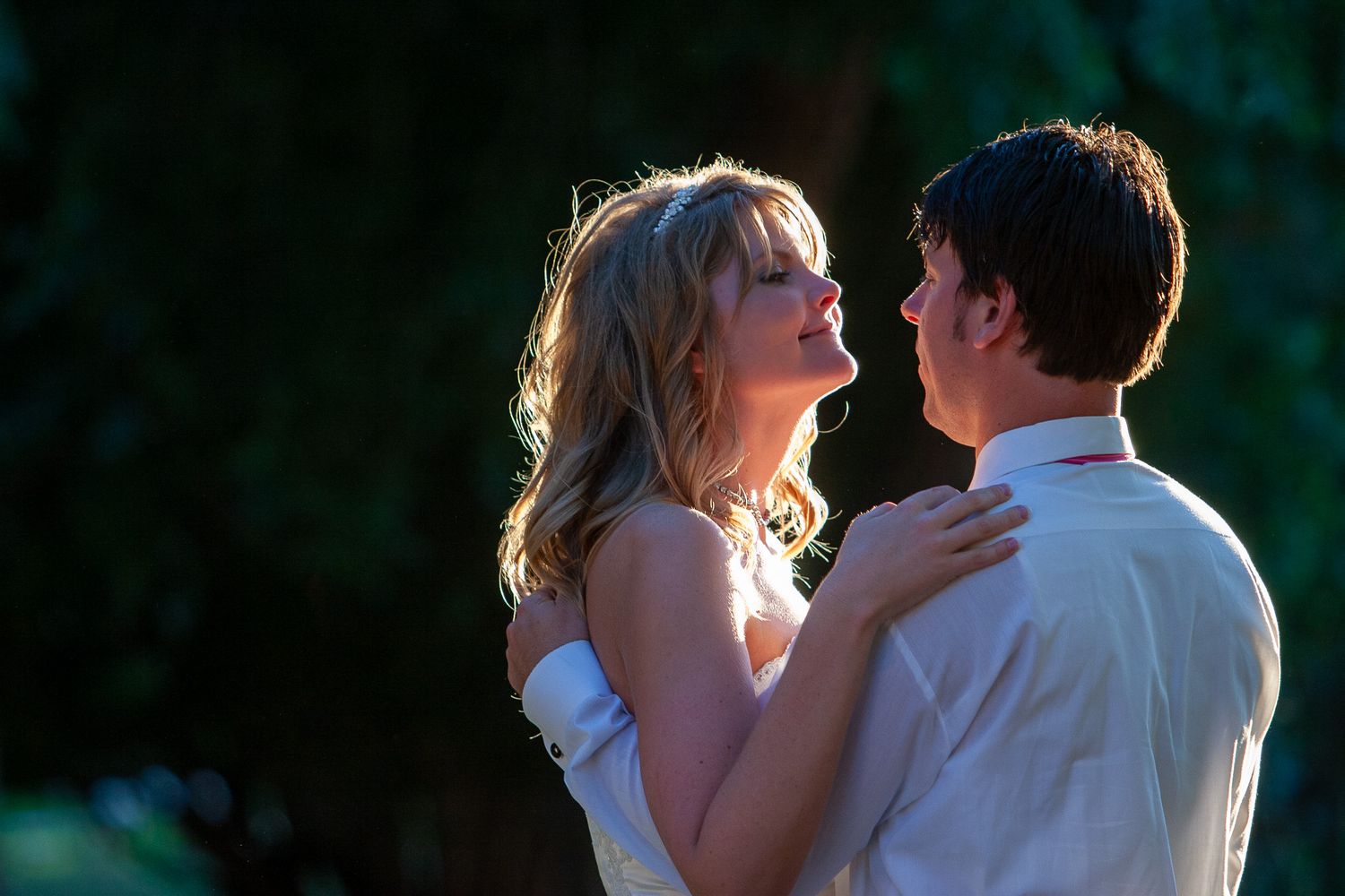A bride and groom share a tender moment dancing outdoors in soft golden light.