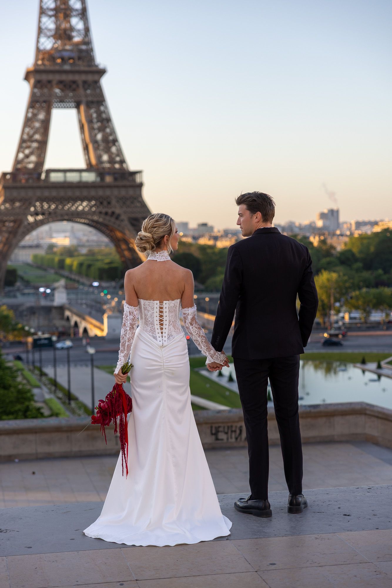 Wedding couple holds hands gazing at the Eiffel Tower at golden hour in Paris.
