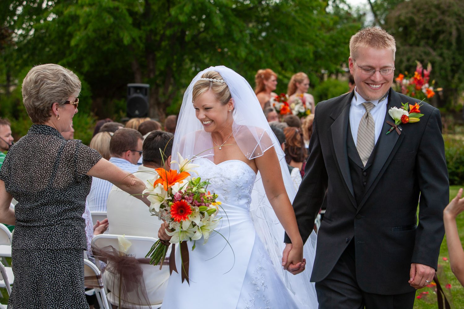 Smiling bride and groom walk hand in hand down the aisle after outdoor wedding ceremony.