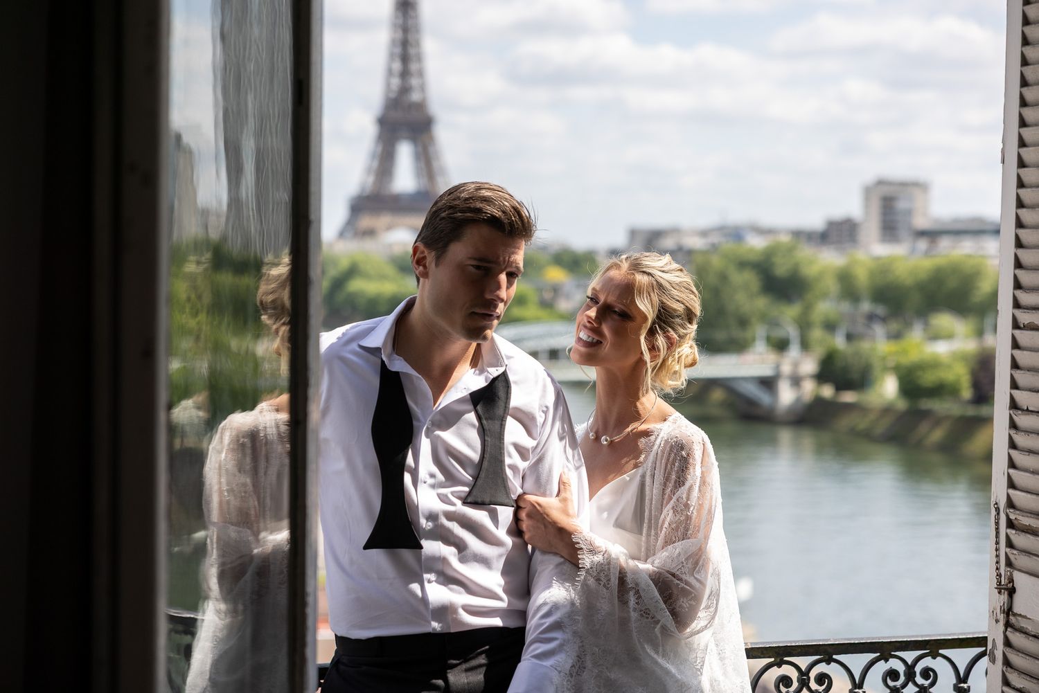 Couple in wedding attire share a romantic moment on Paris balcony with Eiffel Tower.