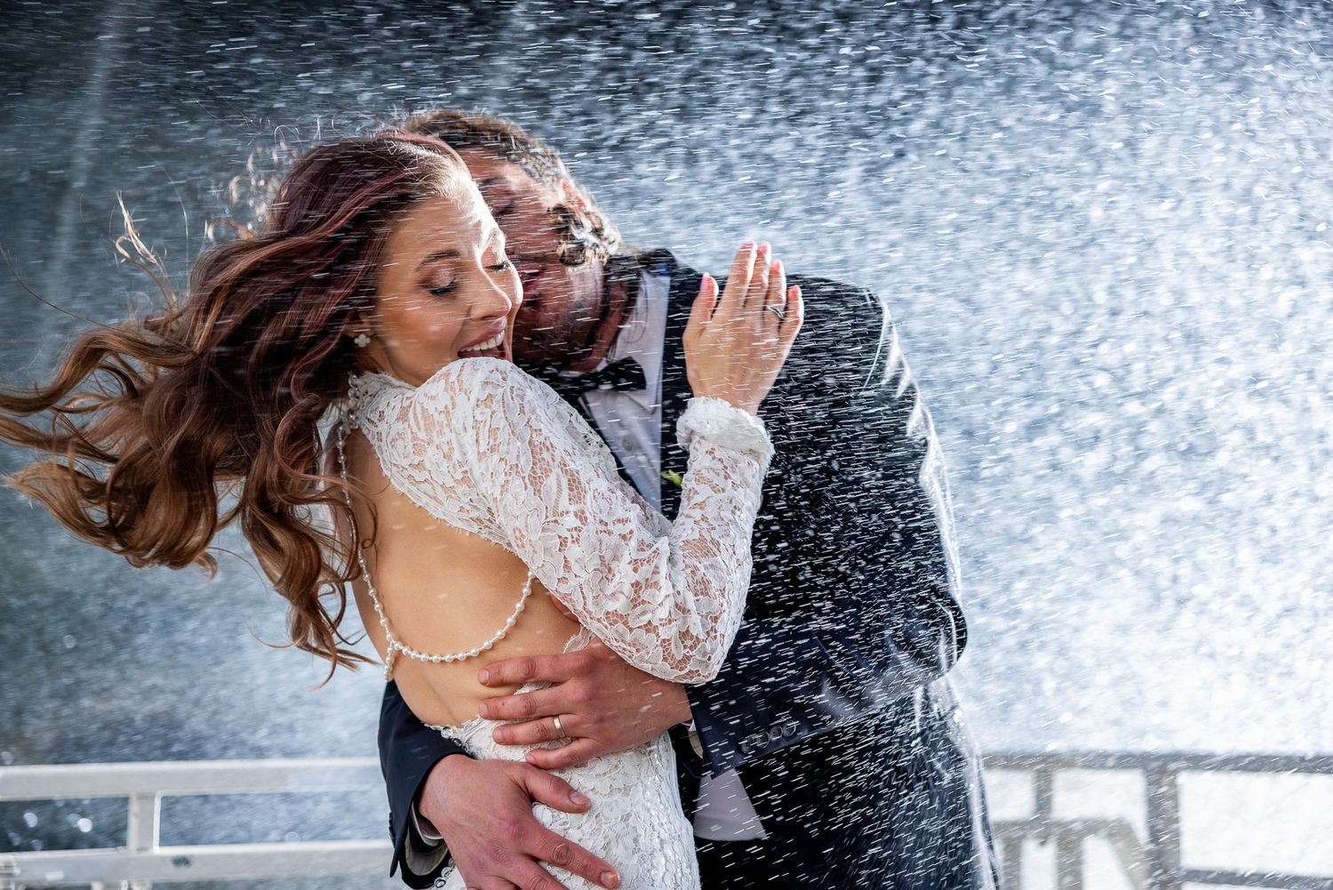 Bride and groom embracing passionately in the rain on their wedding day.