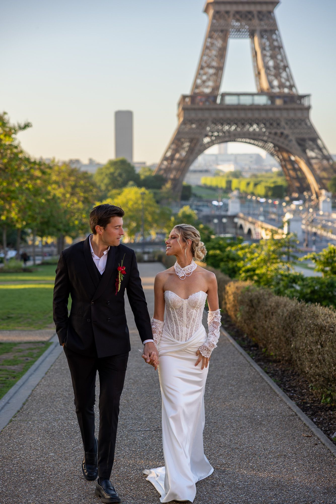 Newlyweds stroll hand in hand along a Paris pathway with the Eiffel Tower behind.