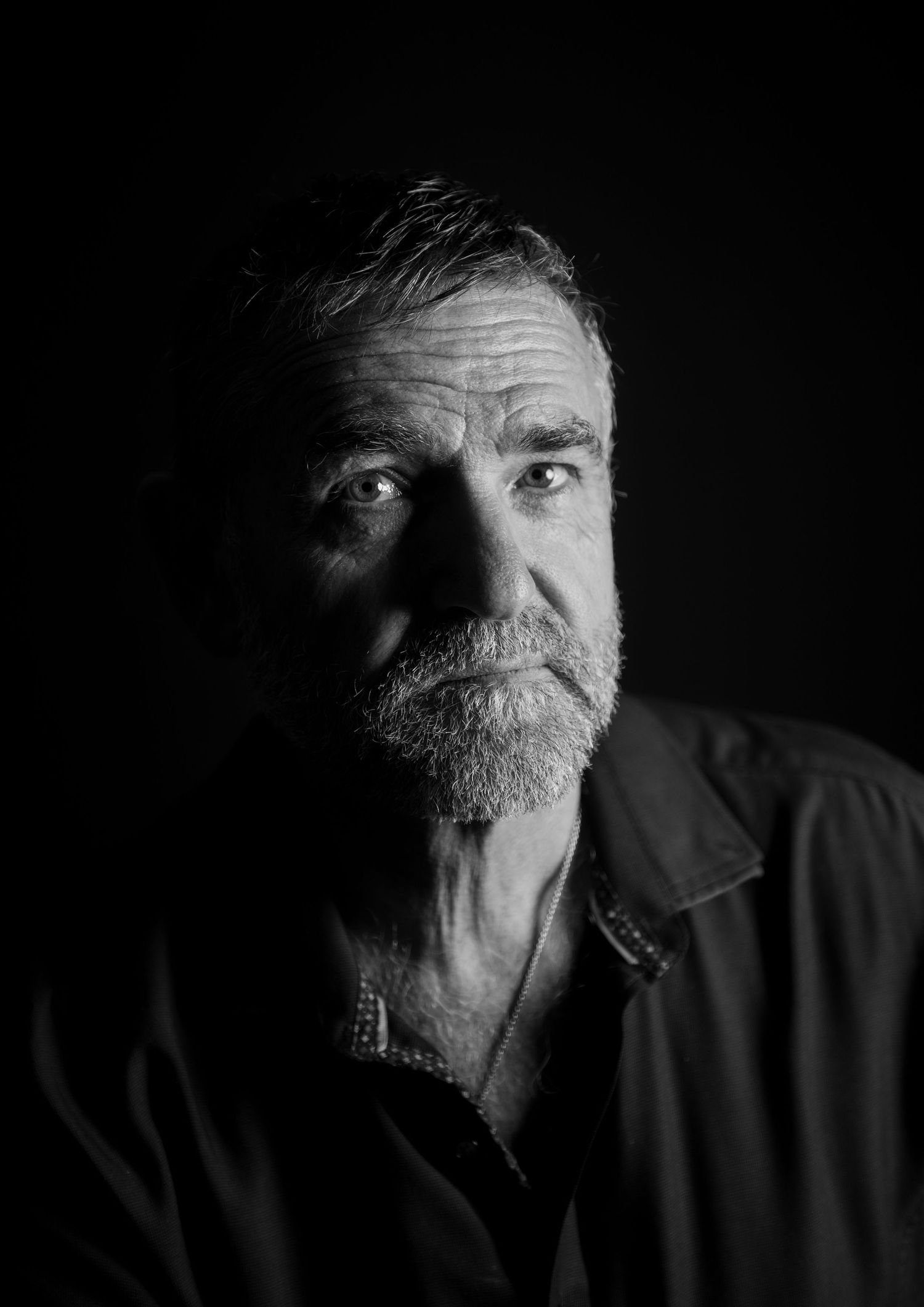 Black and white portrait of an older man with a gray beard and short hair against a dark background.